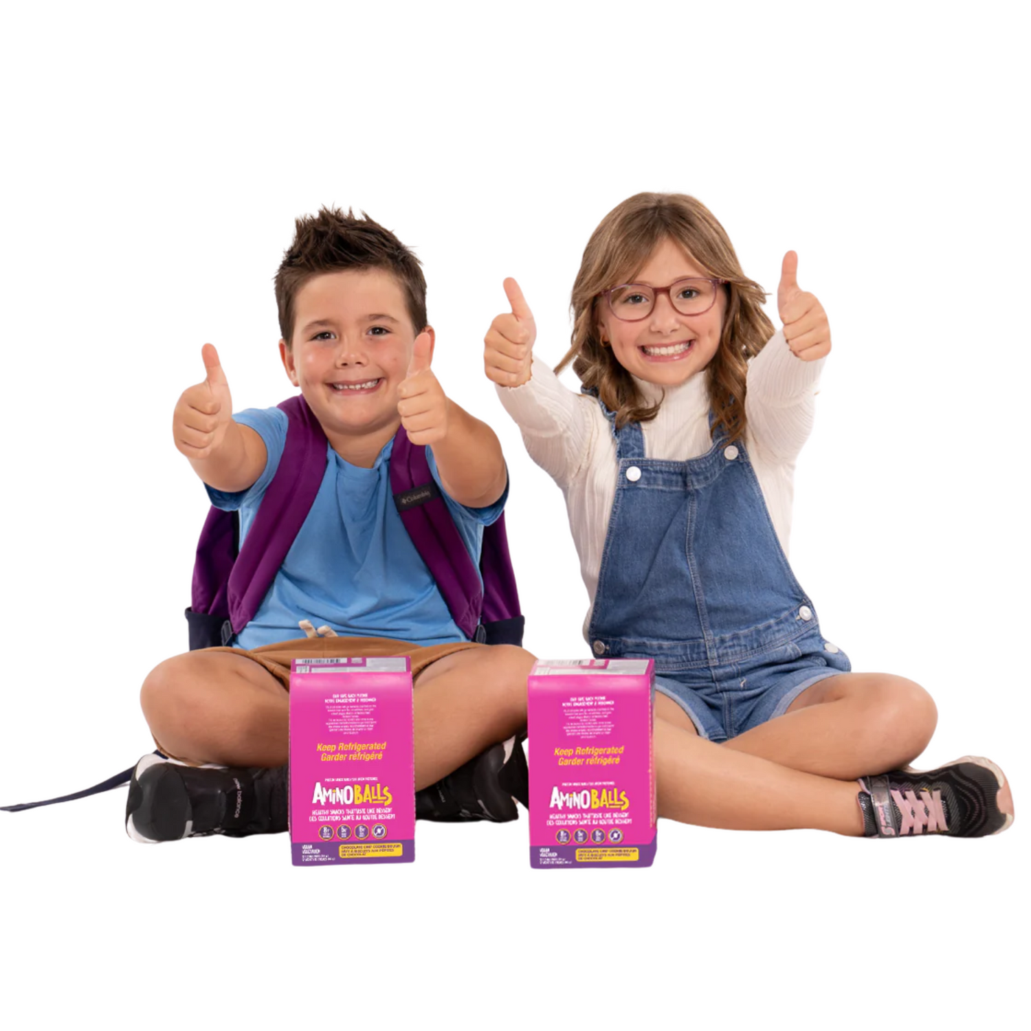 Two kids seated with backpacks on with snacks giving thumbs up